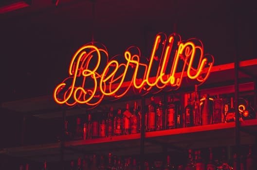 Osvětlený berlínský neonový nápis nad policí lahví alkoholu v prostředí baru.