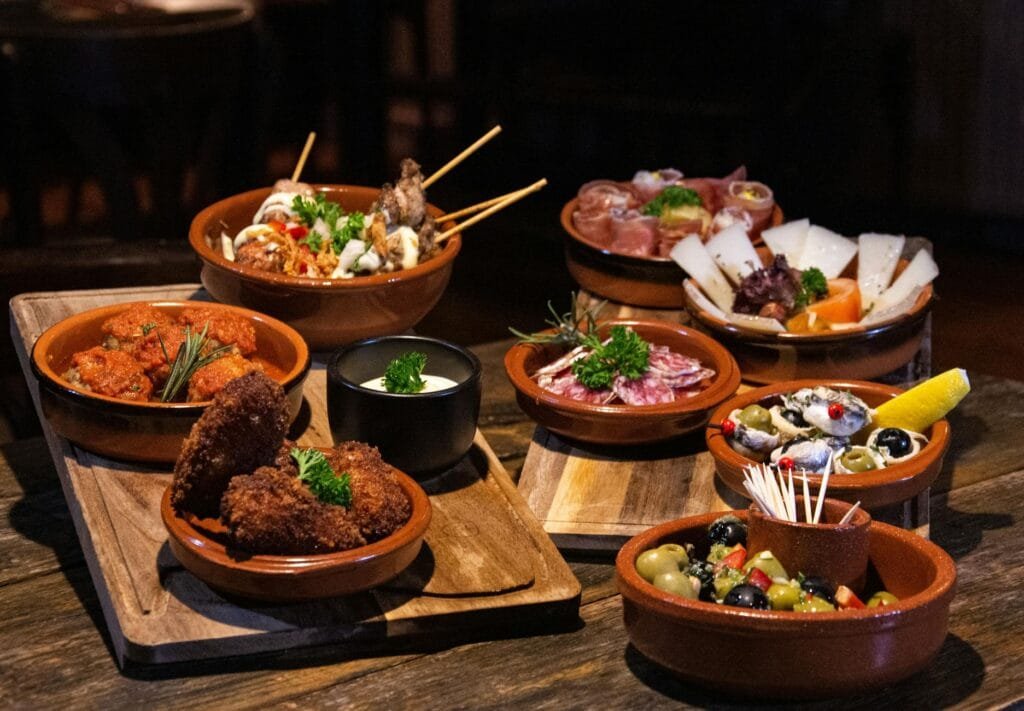 Roztomilá španělská vesnice Mijas láká nejen památkami 2 Assorted Spanish tapas dishes served in rustic style on a wooden table.