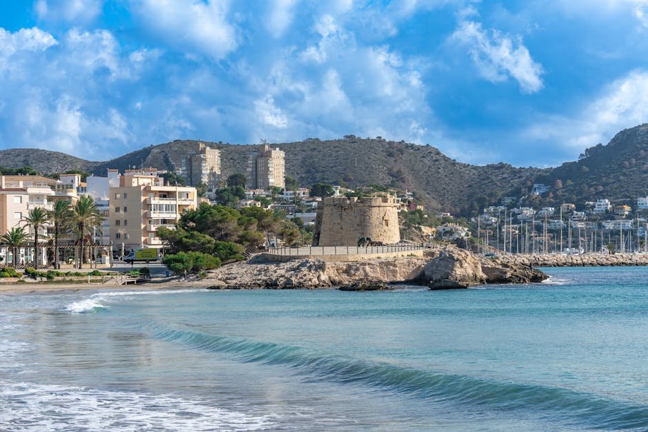 Beautiful coastal view of Moraira beach with historic tower and clear blue sky.