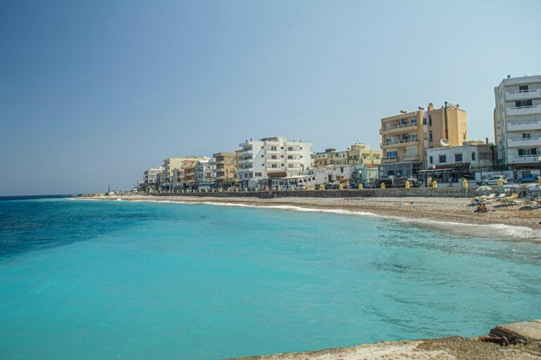 Scenic view of a stunning beach and coastal buildings in Rhodes, Greece under a clear blue sky.