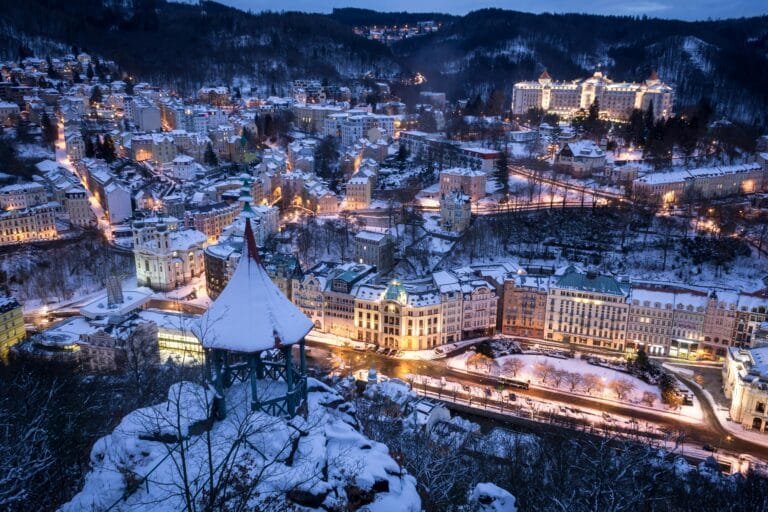 Aerial winter view of Karlovy Vary cityscape at night, showcasing illuminated buildings.