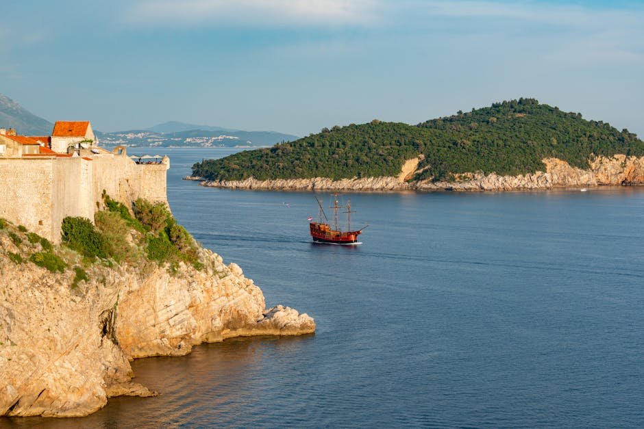 A picturesque view of Dubrovnik's historic coastline with an old ship sailing near a rocky cliff.