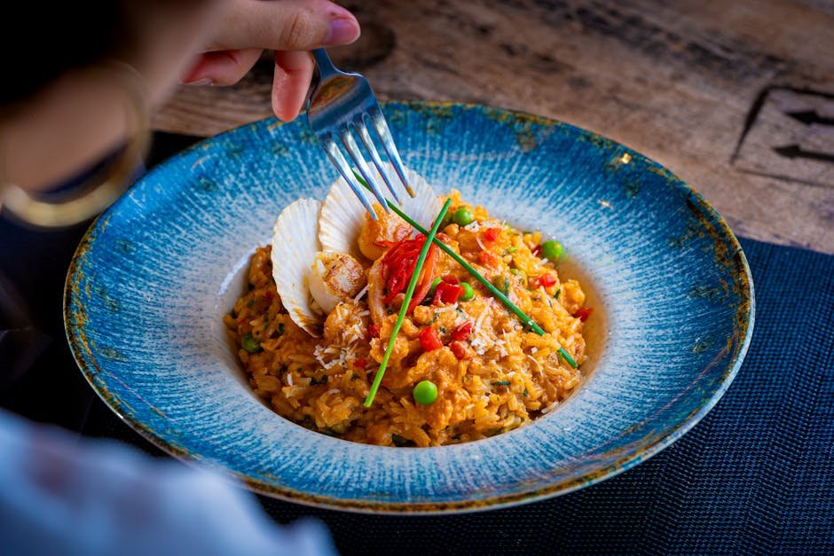 Close-up of seafood paella with vegetables in a blue ceramic bowl being served.