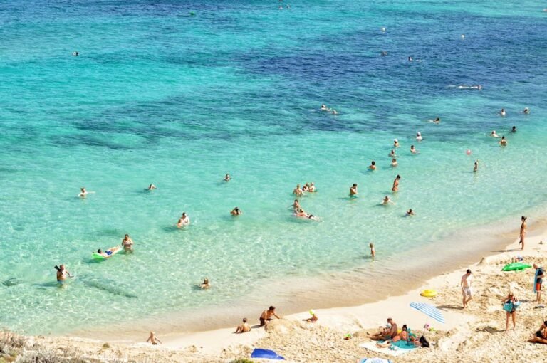 People enjoying a sunny day at a beautiful beach in Mallorca, Spain, with turquoise water and sandy shores.
