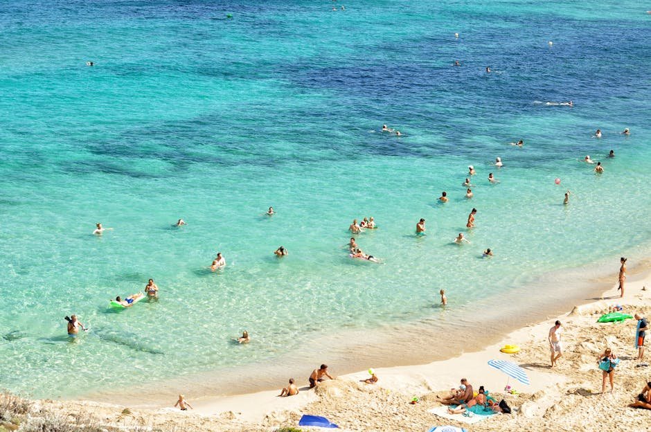 People enjoying a sunny day at a beautiful beach in Mallorca, Spain, with turquoise water and sandy shores.
