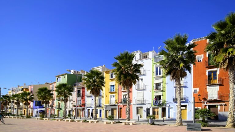 Vibrant seaside buildings in Villajoyosa, Spain with palm trees under a clear blue sky.