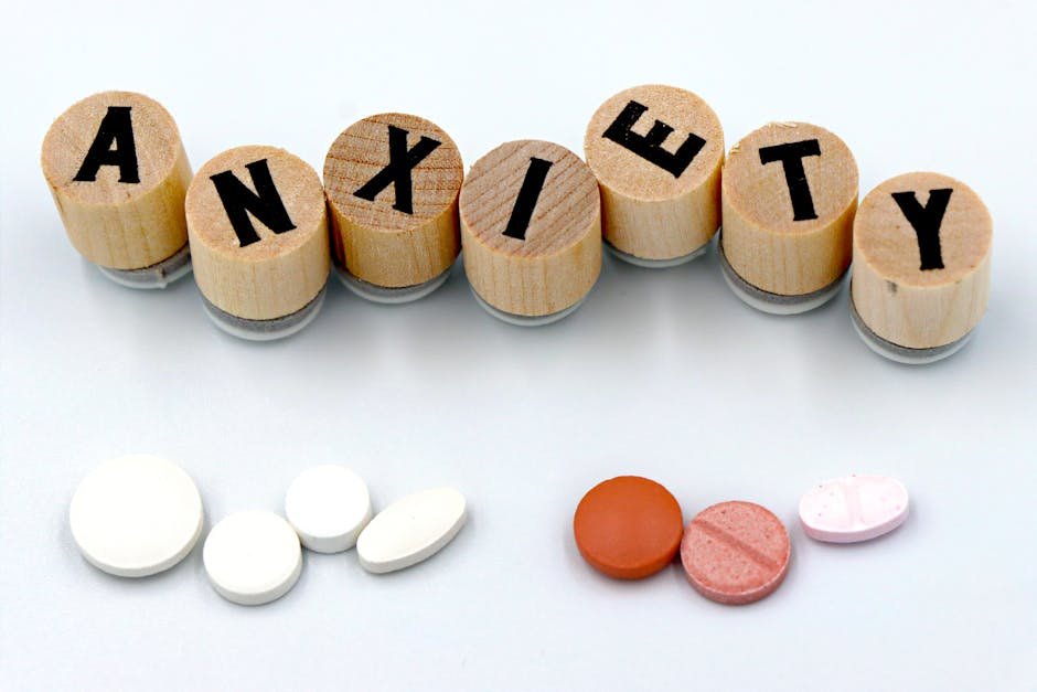 Wooden blocks spelling 'Anxiety' with assorted pills below on a light background.