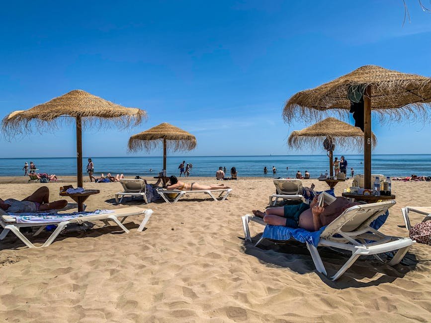 Sunbathers enjoy a sunny day at the beach with straw umbrellas and clear blue sky.