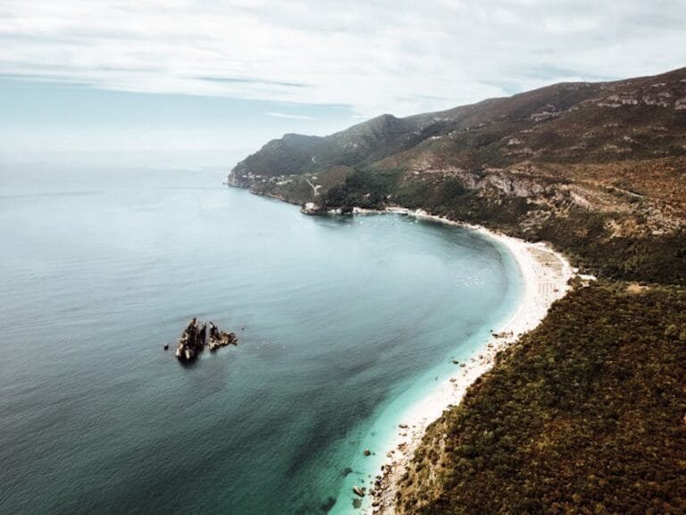 Aerial shot of the scenic Setúbal coastline with lush green mountains and clear ocean waters.