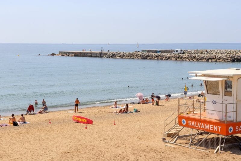 Lively beach scene at Barceloneta in Barcelona, featuring a lifeguard tower and sunbathers.