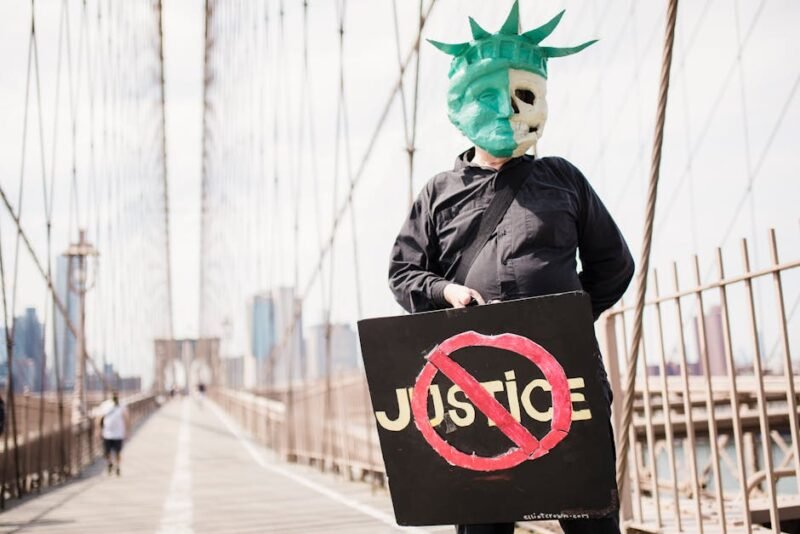 Individual wearing a Statue of Liberty mask holding a justice protest sign on Brooklyn Bridge.