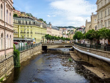 Scenic view of Karlovy Vary's canal with historic buildings and lush greenery under a blue sky.