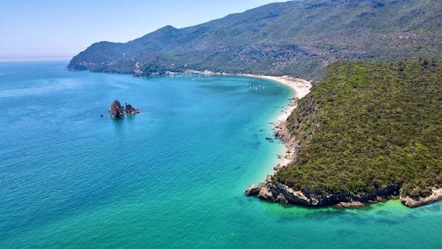 Stunning aerial view of the turquoise waters and lush coastline of Setúbal, Portugal on a bright summer day.