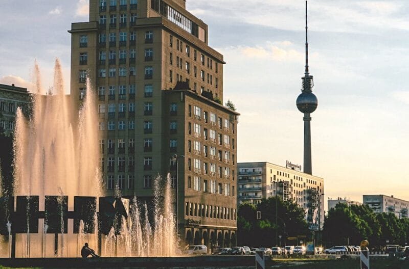 Berlino | Cosa Fare per un Viaggio Indimenticabile Germania 1 Evening view of Berlin's iconic TV Tower, modern buildings, and a lively fountain.