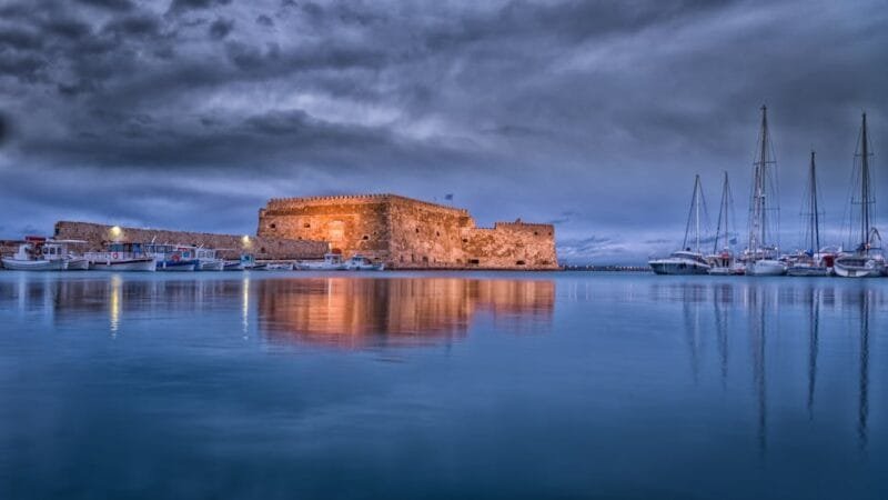 Creta Grecia | La Tua Guida Definitiva all'Isola Verde 1 Majestic view of Koules Fortress reflected in calm waters at Heraklion harbor during twilight.