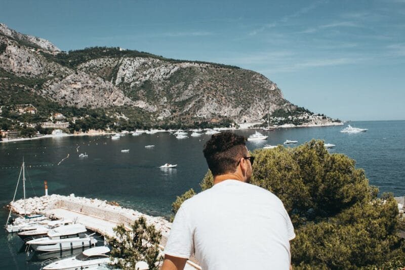 Traveler enjoying the picturesque harbor view at the French Riviera with sailboats and mountains.