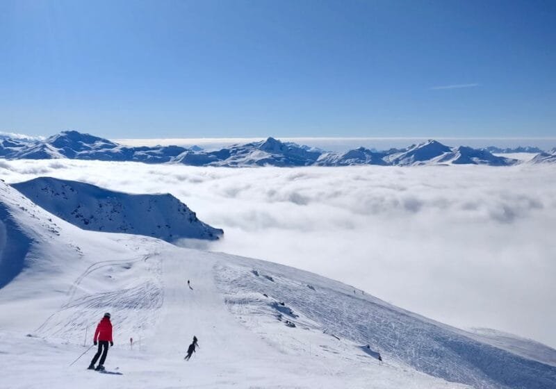 La France | Attrazioni principali e cosa fare il viaggio 4 Skiers enjoy winter slopes at Val Thorens, France with stunning cloud views.