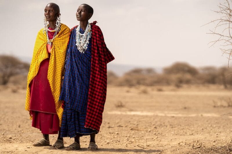 Africa | Un continente pieno di vita e avventure 3 Masai individuals wearing vibrant traditional robes stand in the Tanzanian desert.