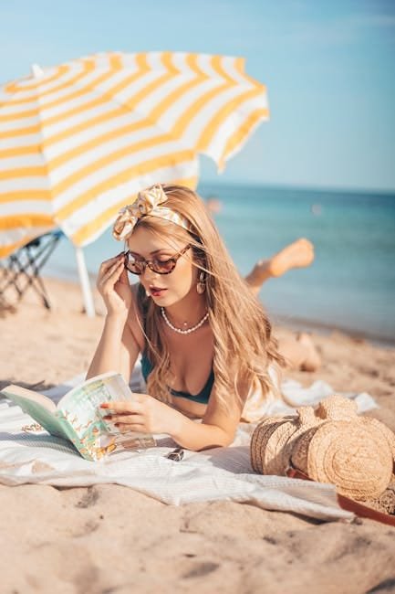 Woman enjoying a book under a sun umbrella on a sandy beach.